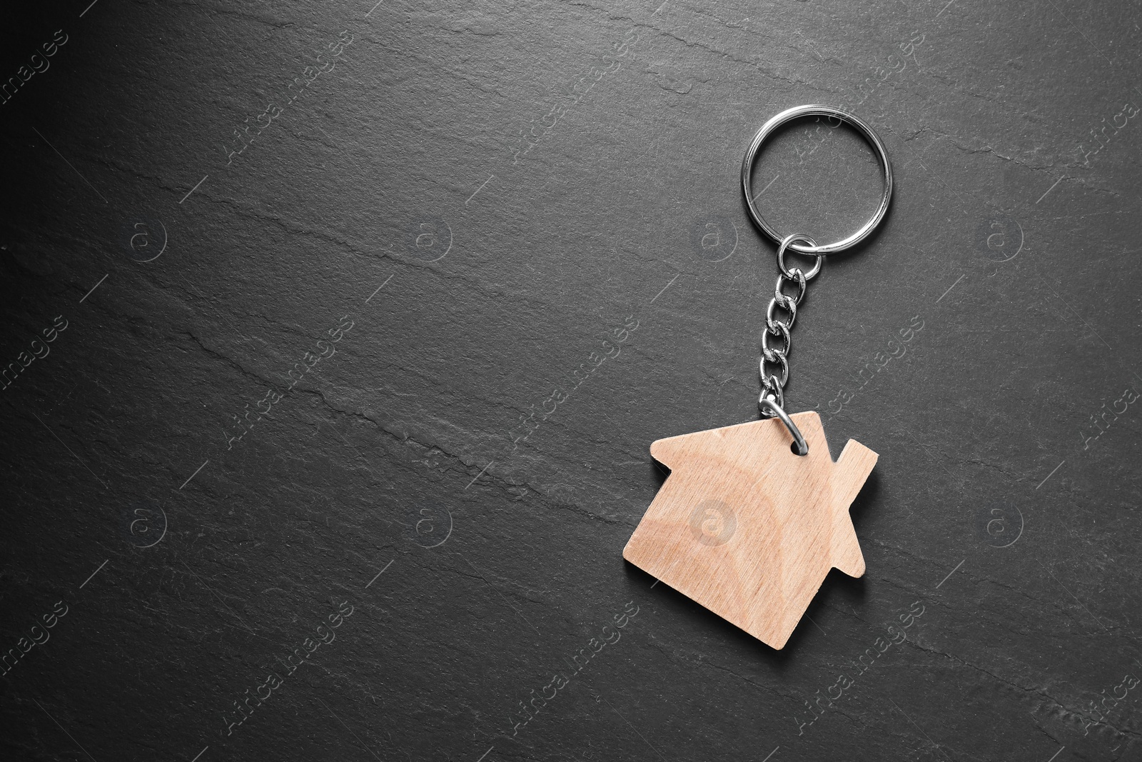 Photo of Wooden keychain in shape of house on dark textured table, top view. Space for text