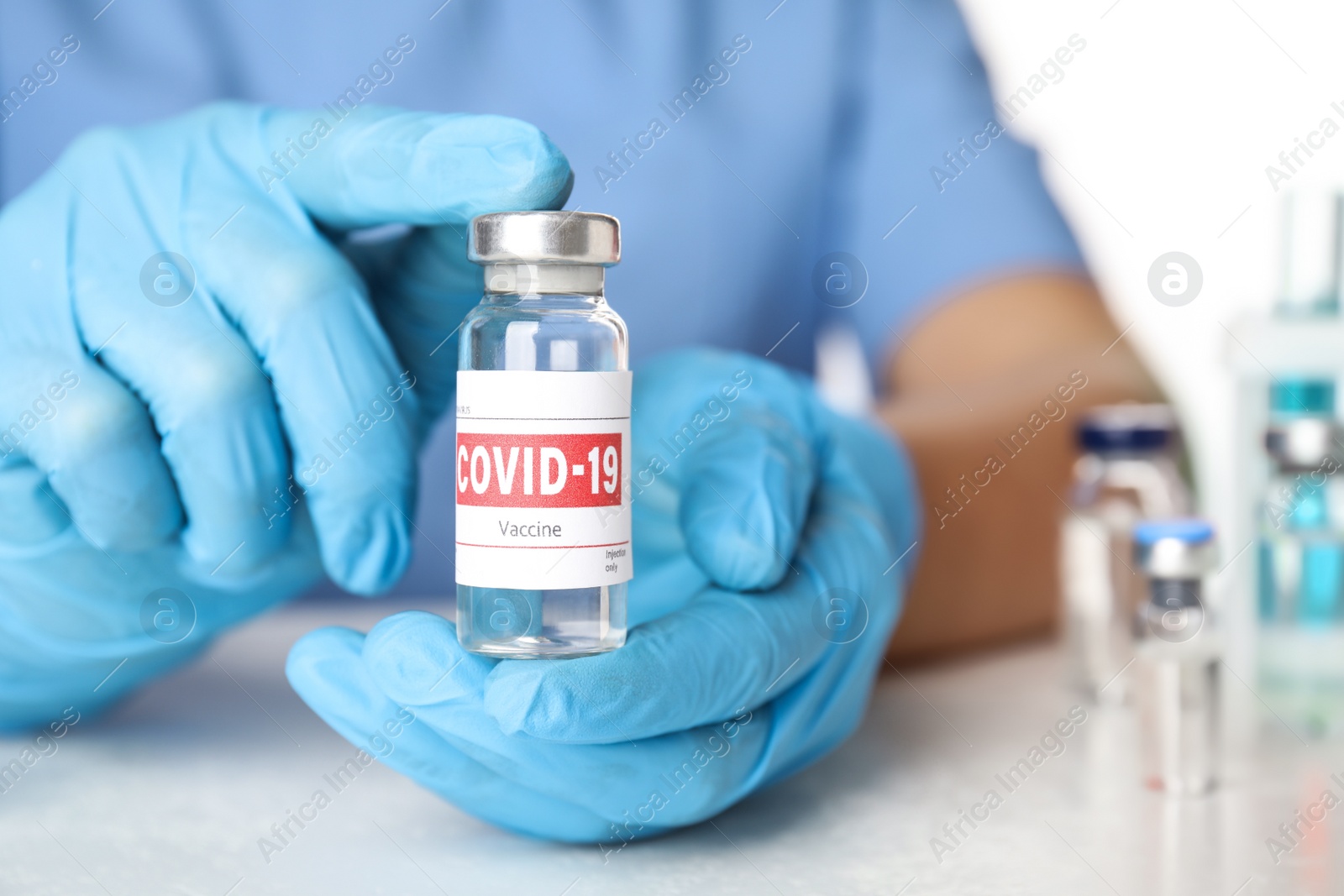 Photo of Doctor holding vial with vaccine against Covid-19 at table, closeup