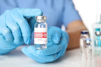Photo of Doctor holding vial with vaccine against Covid-19 at table, closeup