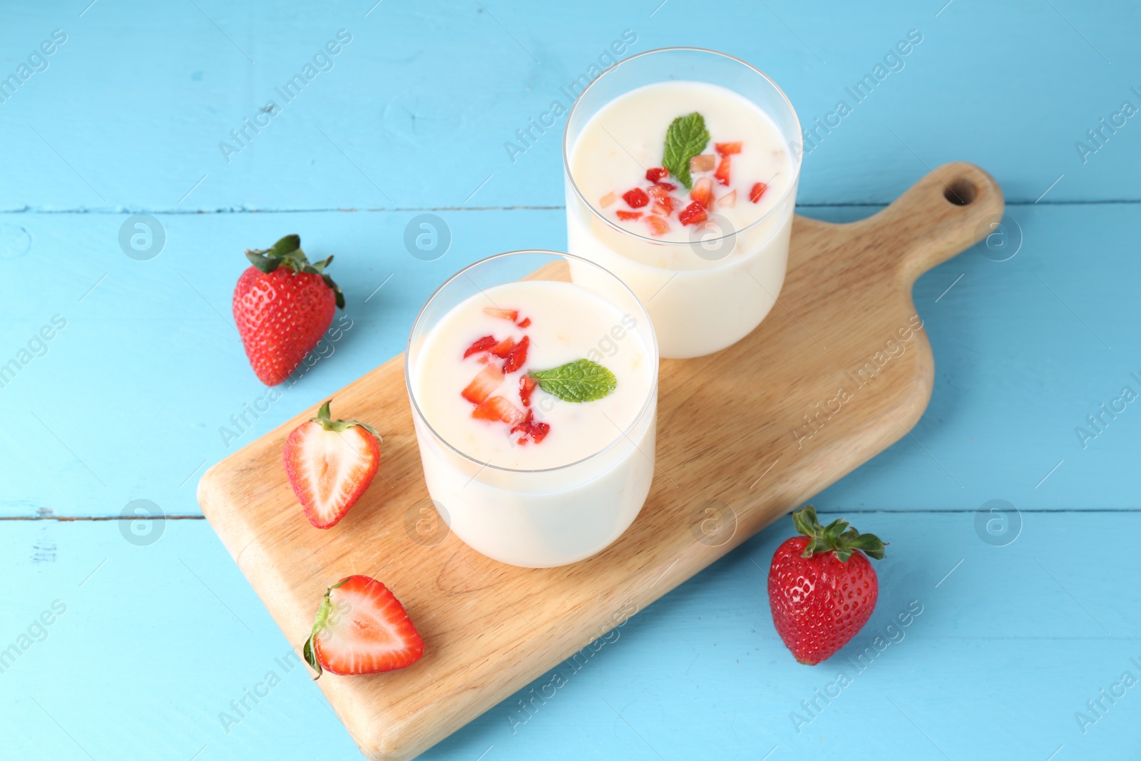 Photo of Tasty yogurt in glasses and strawberries on light blue wooden table