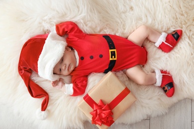 Photo of Cute baby in Christmas costume with gift box lying on fur rug