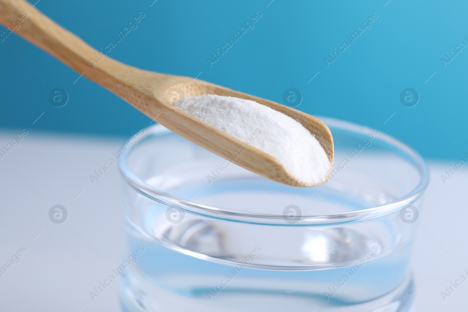 Photo of Spoon with baking soda over glass of water on color background, closeup