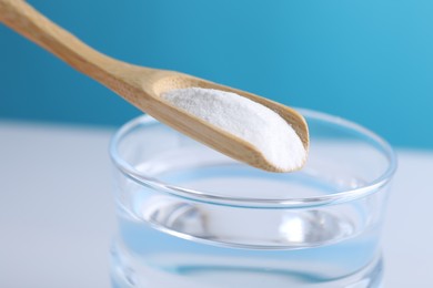 Photo of Spoon with baking soda over glass of water on color background, closeup