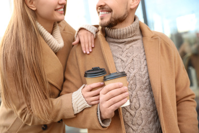 Photo of Couple with cups of coffee on city street in morning, closeup
