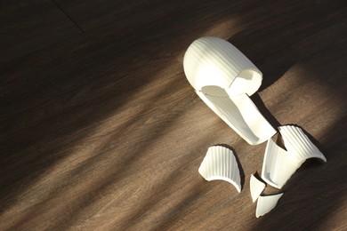 Photo of Broken white ceramic vase on wooden floor, above view. Space for text