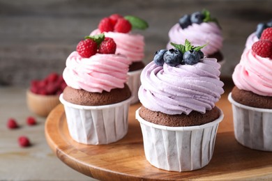 Sweet cupcakes with fresh berries on wooden plate, closeup