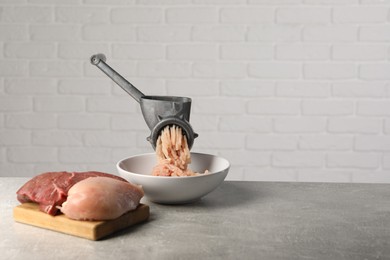 Photo of Metal meat grinder with mince, raw chicken and beef on grey table near light wall. Space for text