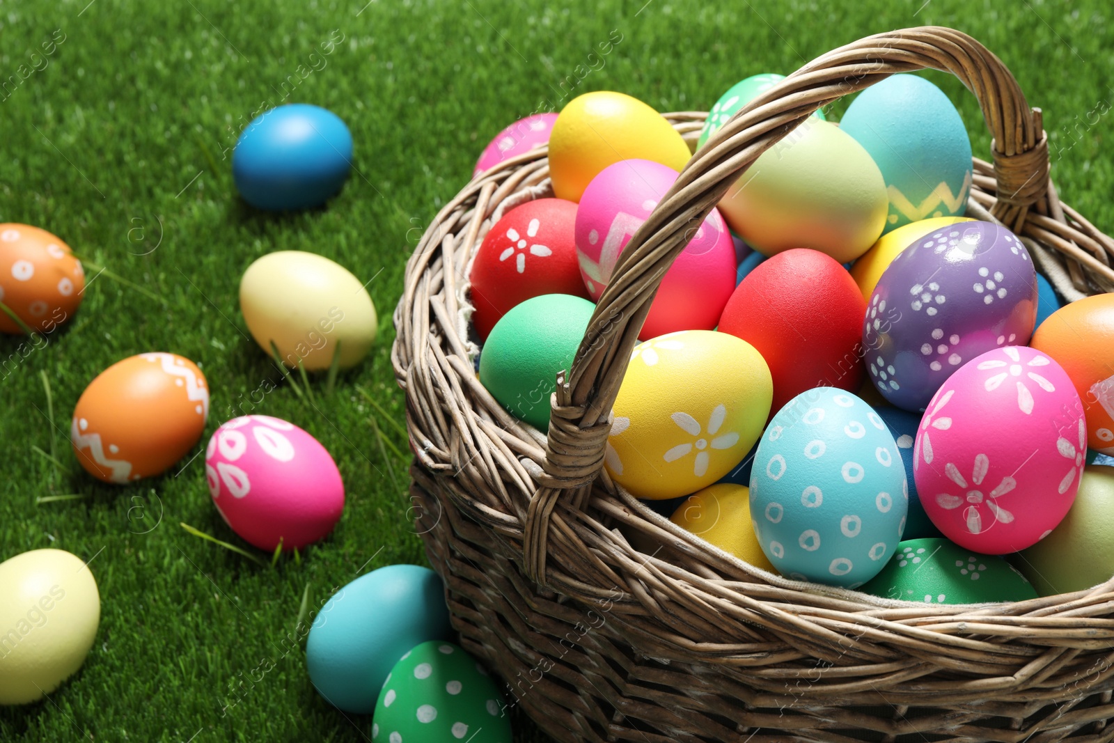 Photo of Colorful Easter eggs in basket on green grass