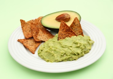 Photo of Delicious guacamole, avocado and nachos on light green background, closeup