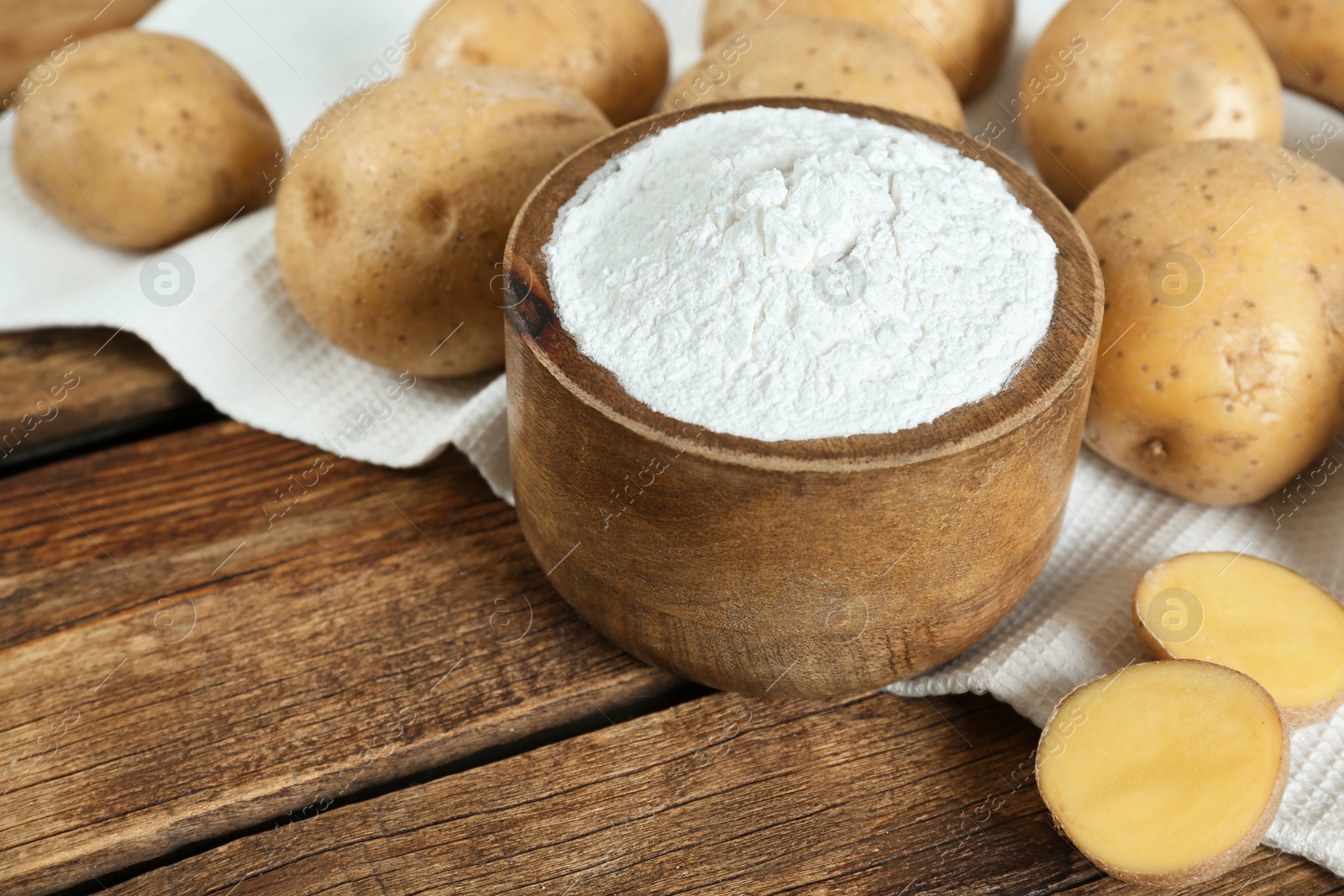 Photo of Starch and fresh raw potatoes on wooden table