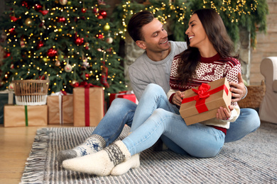 Photo of Happy couple with gift box in living room decorated for Christmas