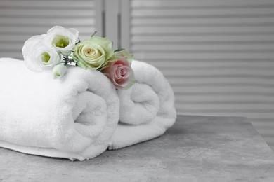 Photo of Rolled towels and flowers on grey table indoors, space for text