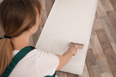 Photo of Worker applying glue onto wall paper sheet, focus on hand