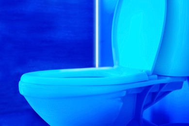 Image of Toilet bowl in public restroom lit with UV blue light, closeup view