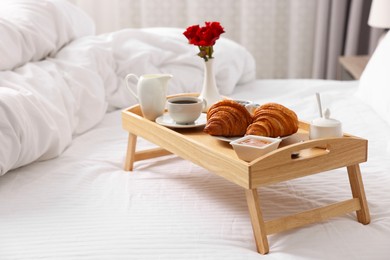 Photo of Wooden tray with tasty breakfast on bed at home