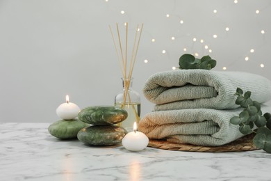 Photo of Spa composition. Herbal massage bags, stones, reed air freshener and burning candles on white marble table, space for text