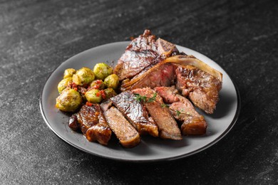 Photo of Delicious fried beef meat, vegetables and thyme on black table, closeup