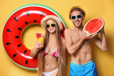 Young couple in beachwear with inflatable ring and watermelon on color background