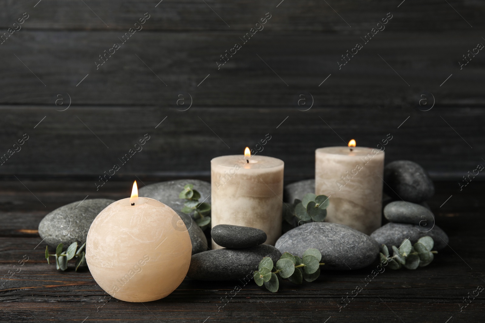 Photo of Composition with burning candles, spa stones and eucalyptus on dark wooden table