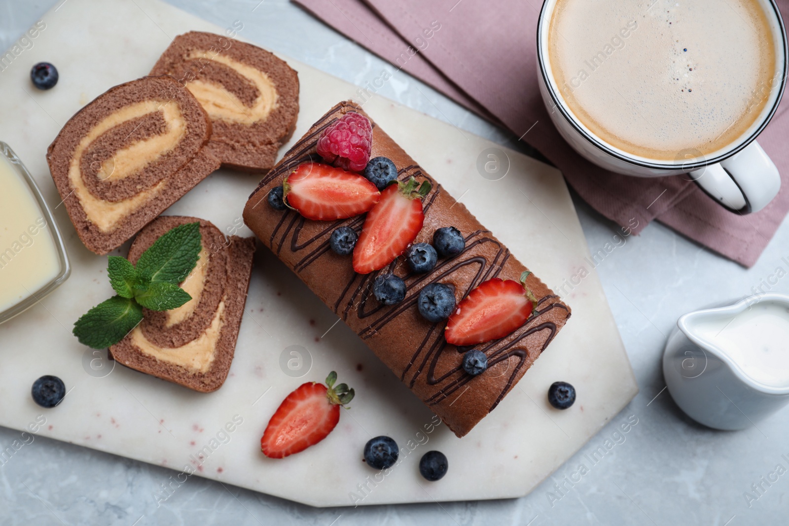 Photo of Tasty chocolate cake roll with cream and berries on light grey marble table, flat lay