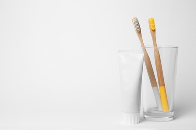 Photo of Glass with brushes and toothpaste on white background. Space for text