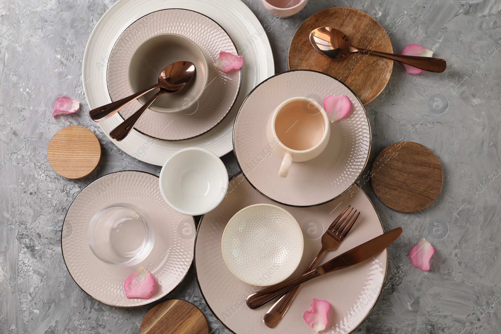Photo of Stylish table setting. Dishes, cutlery, cup and petals on grey surface, flat lay