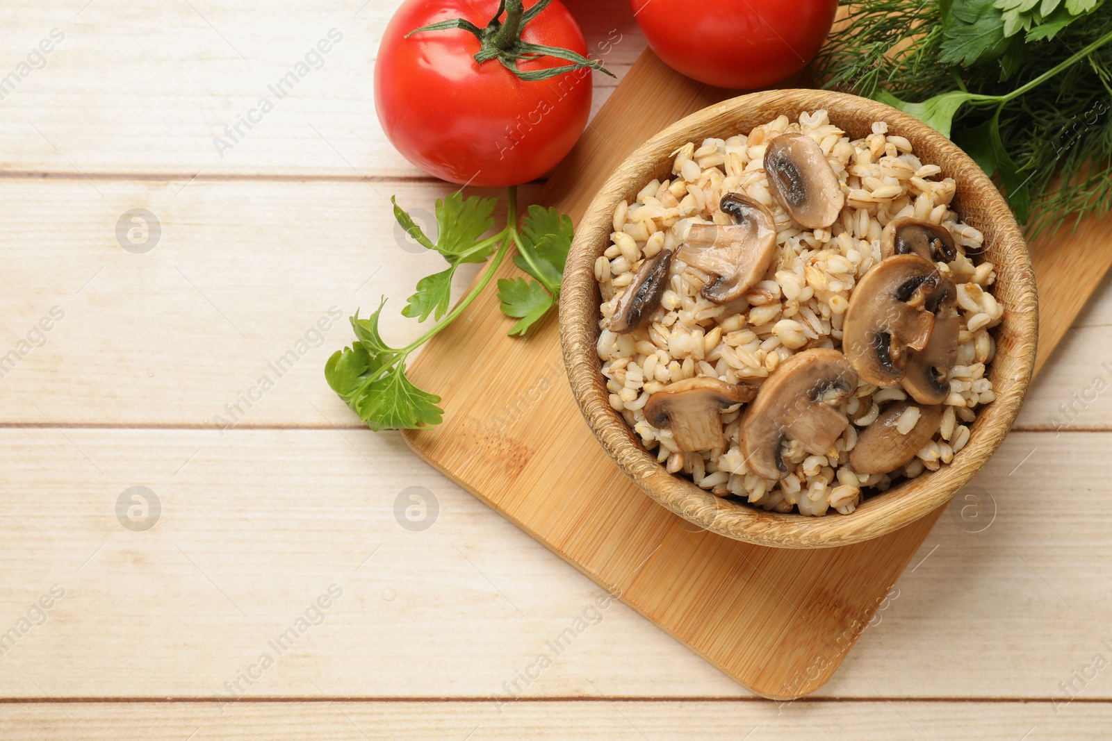 Photo of Delicious pearl barley with mushrooms, parsley and tomatoes on wooden table, top view. Space for text