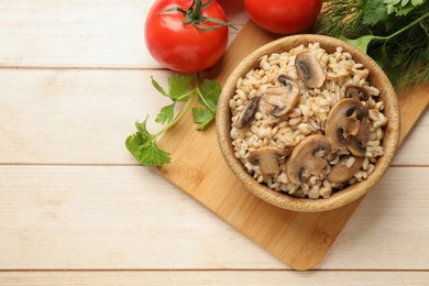 Delicious pearl barley with mushrooms, parsley and tomatoes on wooden table, top view. Space for text