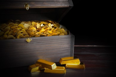 Image of Open treasure chest with coins and gold bars on wooden table, closeup 