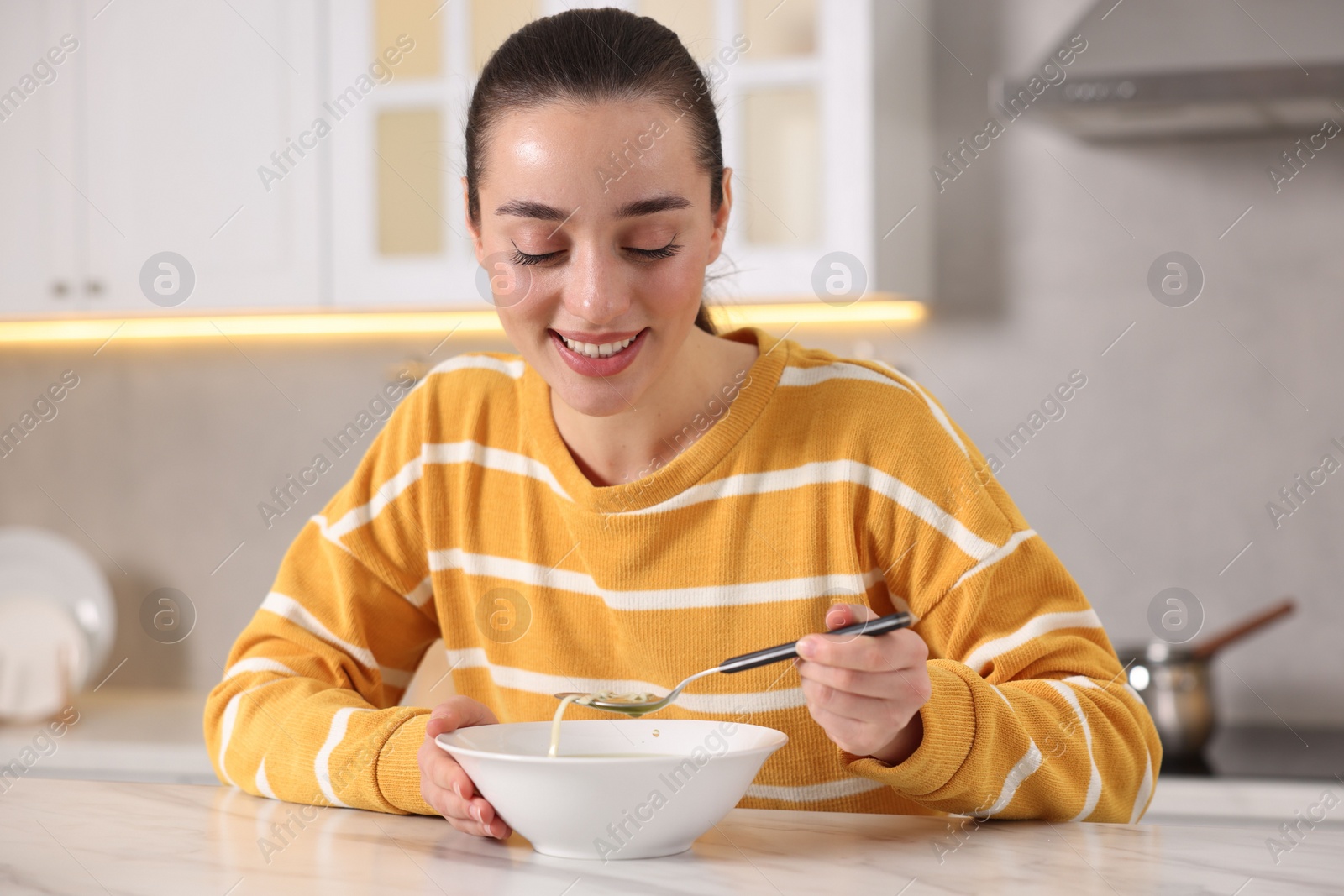 Photo of Woman eating tasty soup at white table in kitchen