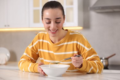 Woman eating tasty soup at white table in kitchen