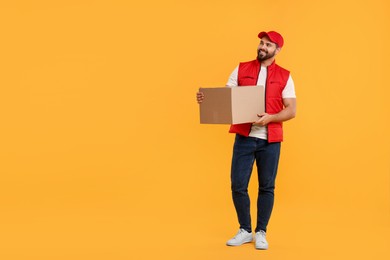 Happy young courier with parcel on orange background. Space for text