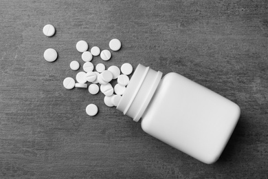 Photo of Bottle with different pills on grey background, flat lay