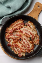 Delicious bacon slices in frying pan on white table, top view