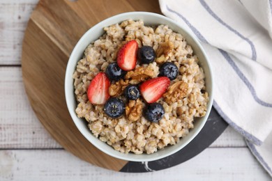 Photo of Tasty oatmeal with strawberries, blueberries and walnuts in bowl on white wooden table, top view