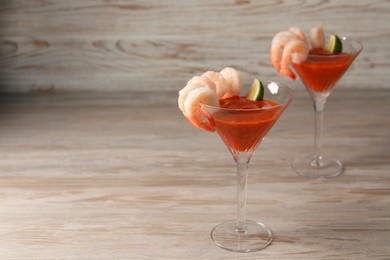 Photo of Tasty shrimp cocktail with sauce and lime in glasses on wooden table, space for text