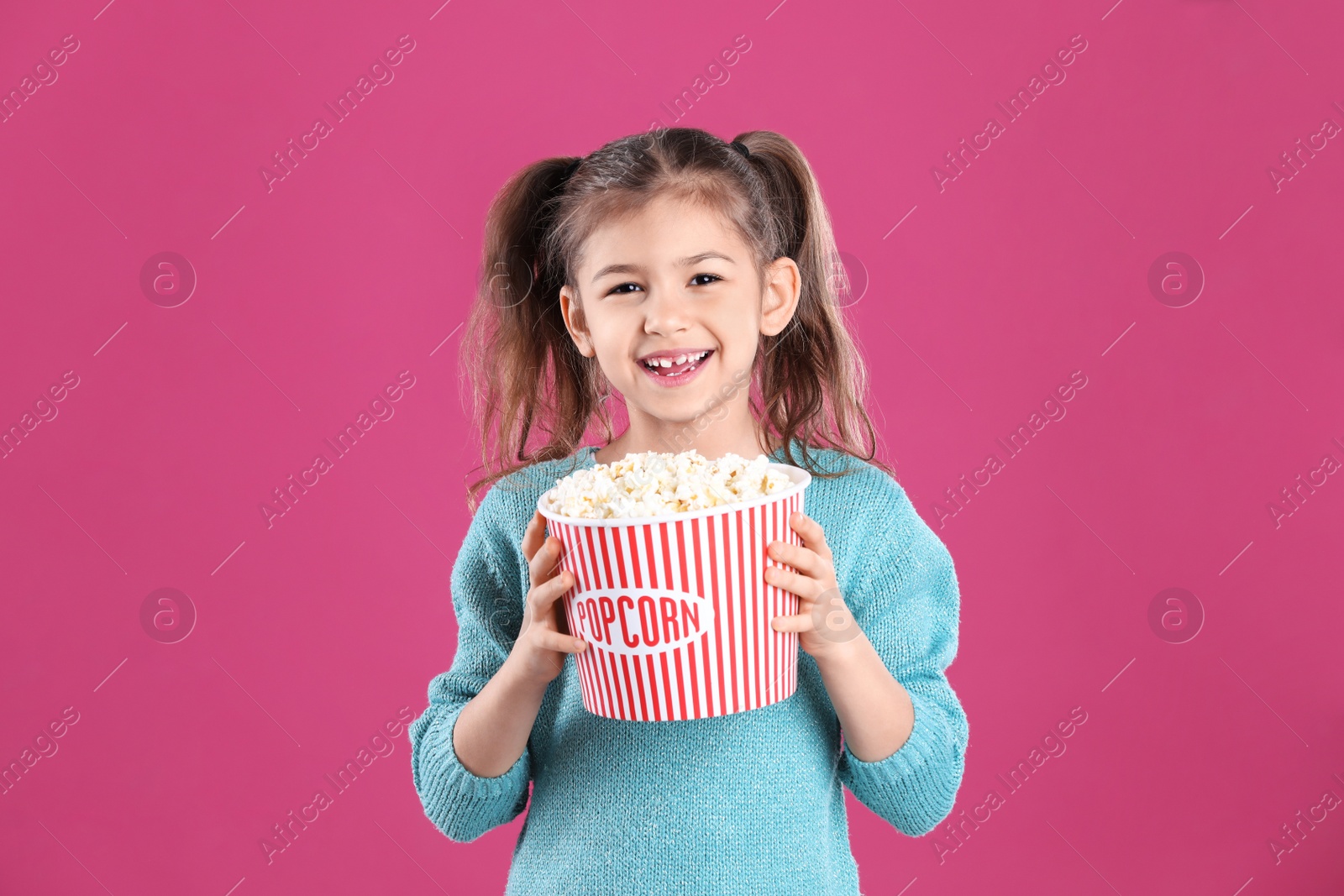 Photo of Cute little girl with popcorn on color background