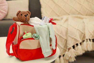 Photo of Mother's bag with baby's stuff on white table indoors. Space for text