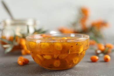 Photo of Delicious sea buckthorn jam and fresh berries on grey table, closeup
