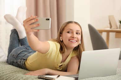 Teenage girl taking selfie on bed at home