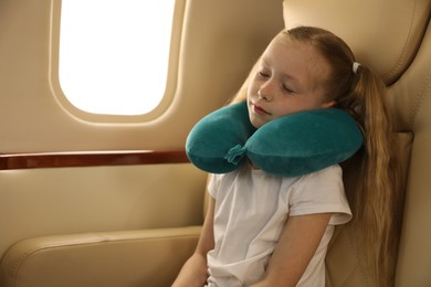 Photo of Cute little girl with travel pillow sleeping in airplane during flight
