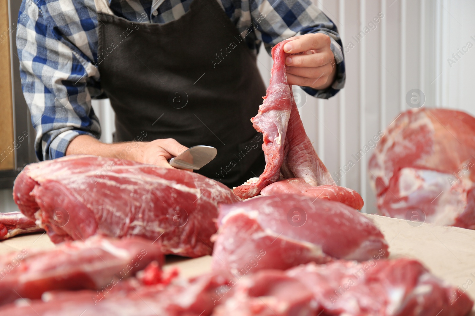 Photo of Butcher cutting fresh raw meat on counter in shop, closeup