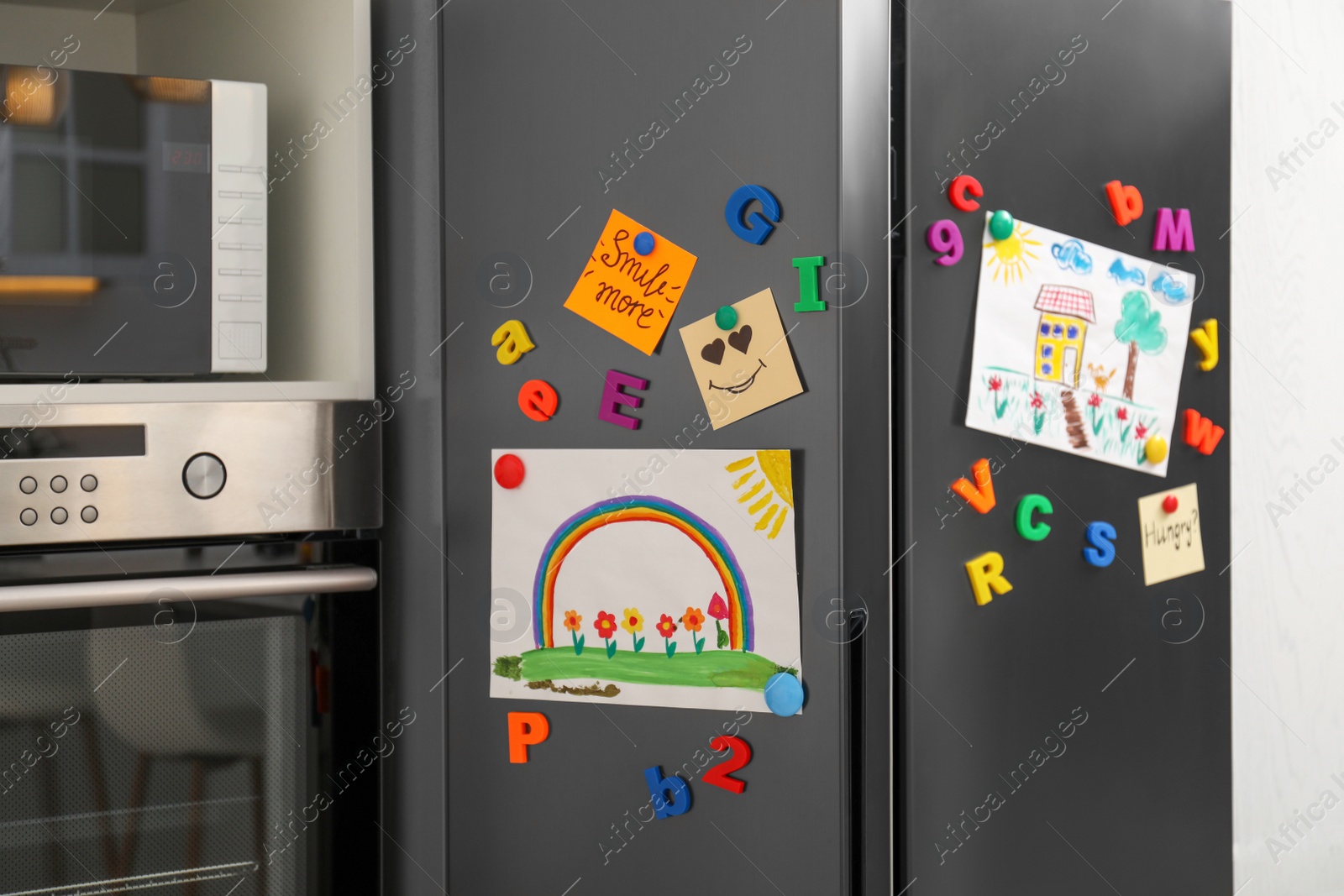 Photo of Modern refrigerator with child's drawings, notes and magnets in kitchen