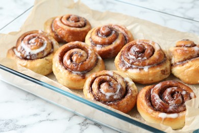 Photo of Baking dish with tasty cinnamon rolls on white marble table, closeup