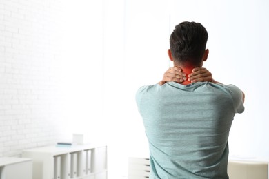 Man suffering from neck pain indoors, back view