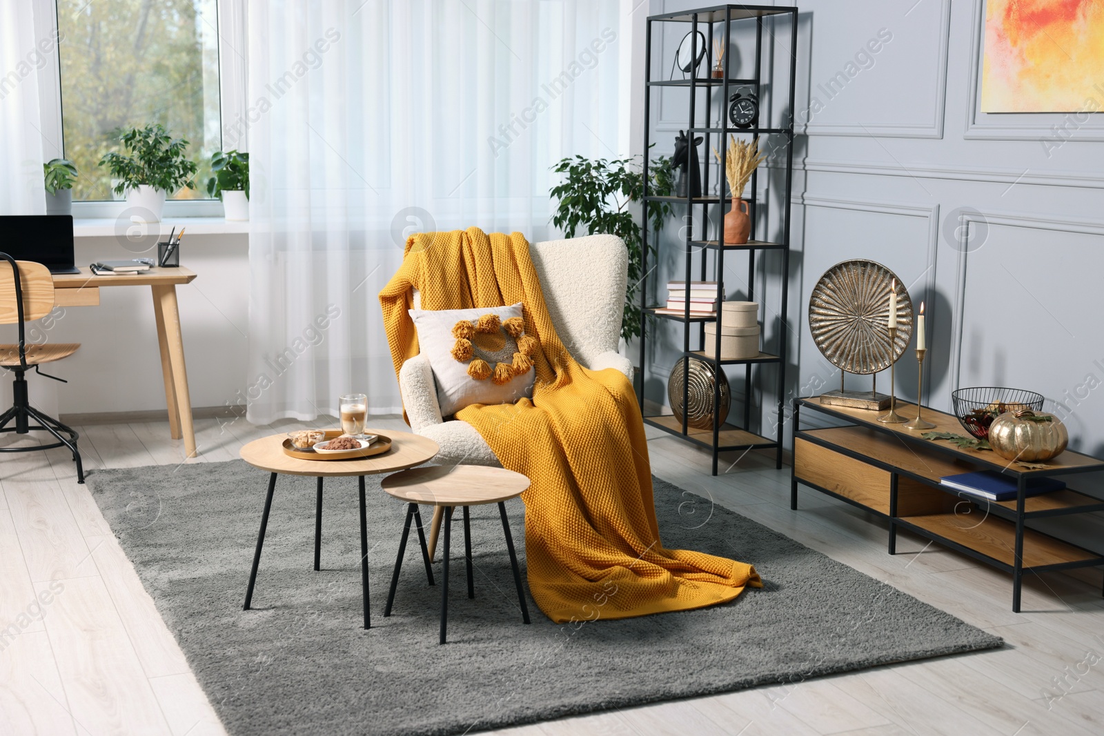 Photo of Stylish room interior with comfortable armchair, blanket and nesting tables