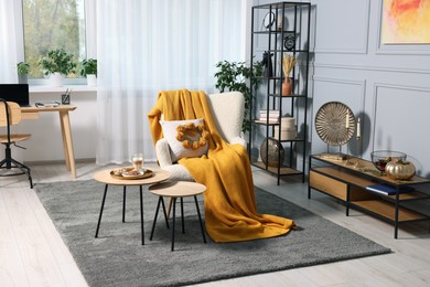 Photo of Stylish room interior with comfortable armchair, blanket and nesting tables