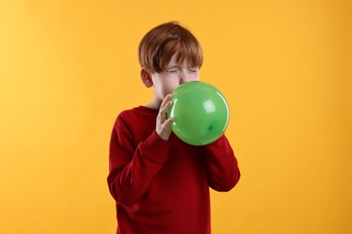 Photo of Boy inflating green balloon on orange background