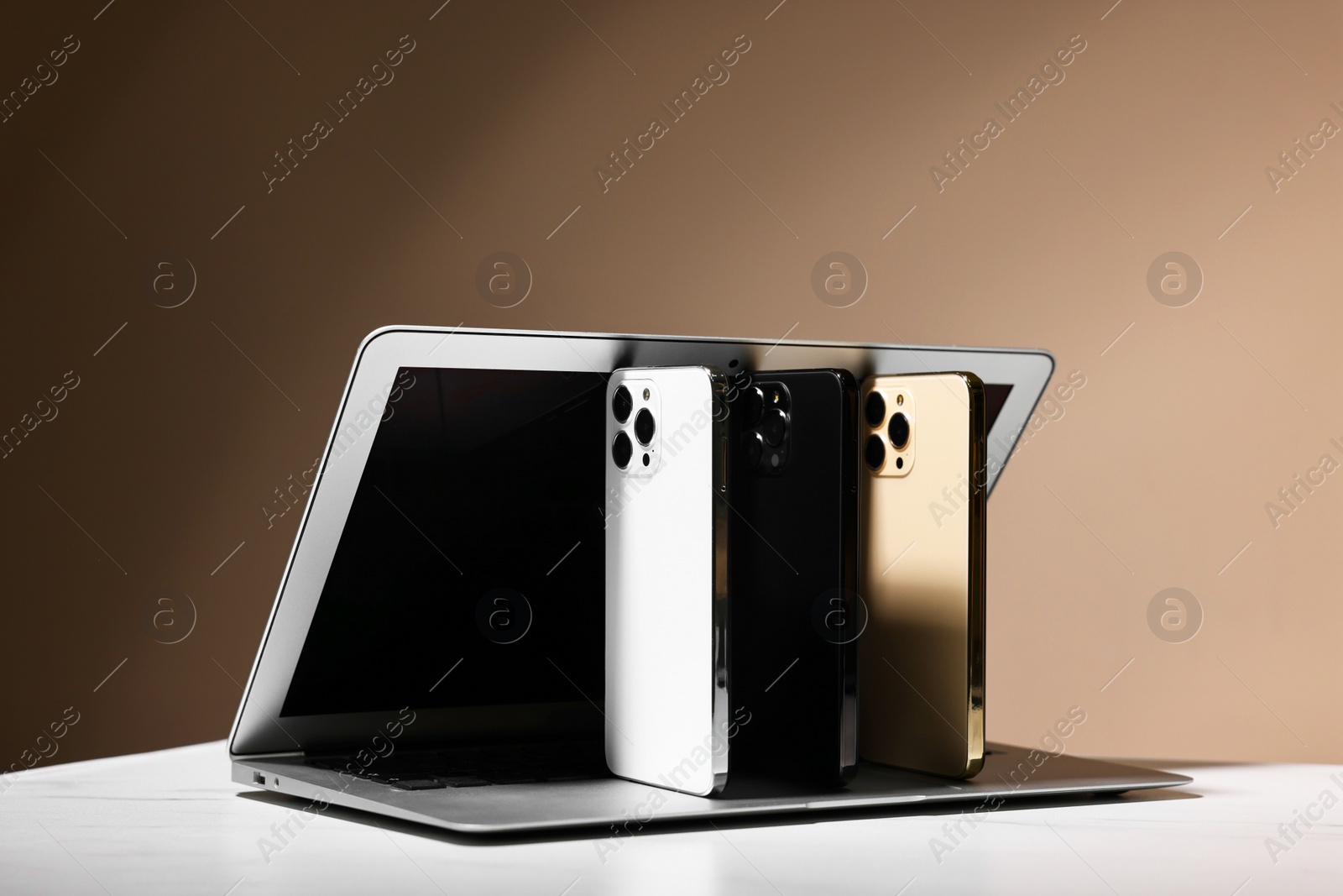 Photo of Modern laptop and smartphones on white table against brown background