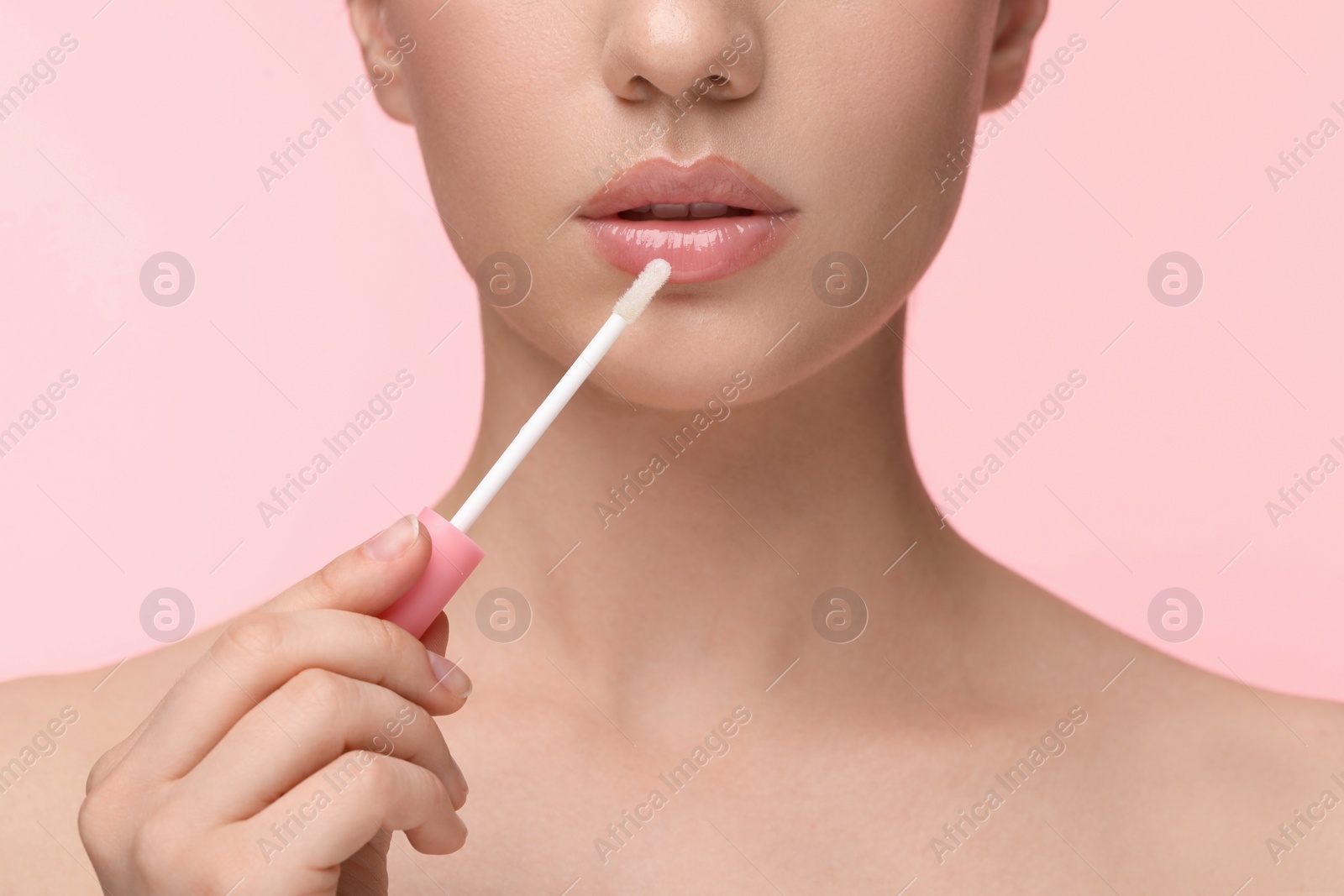 Photo of Woman applying lip gloss on pink background, closeup